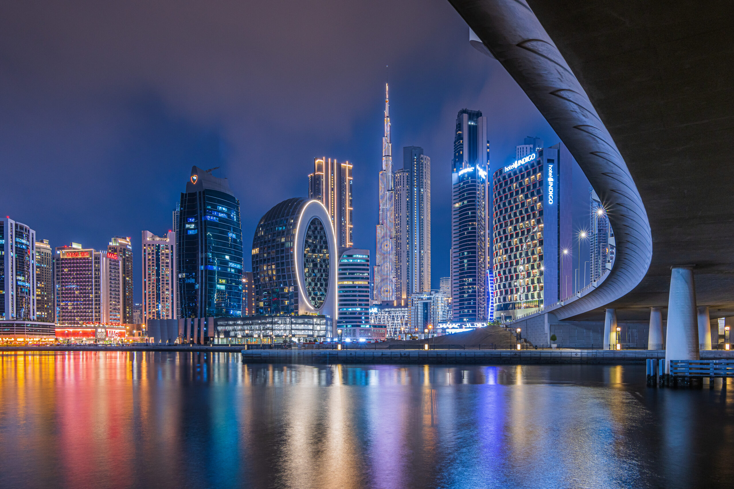 Dubai at night. City skyline in United Arab Emirates. Skyscrapers illuminated at the blue hour with a curved course of a bridge. Reflections on the water surface in the port